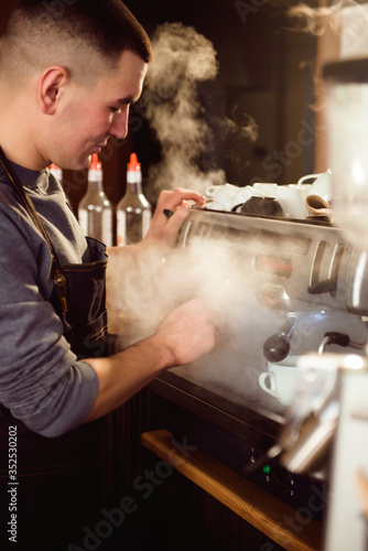 Smiling male barista using professional coffee machine enjoying job in cafe improving skills of making cappuccino