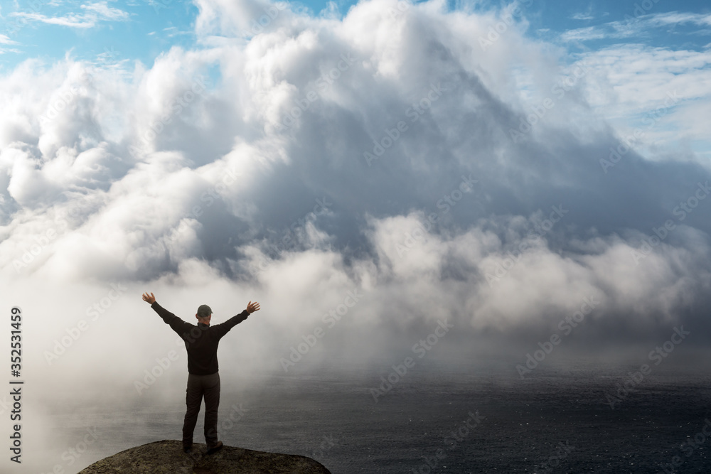 Silhouette of a man with arms raised standing on the edge of a cliff above a foggy ocean. Travel concept. Landscape photography Silhouette of a man with arms raised standing on the edge of a cliff above a foggy ocean. Travel concept. Landscape photography