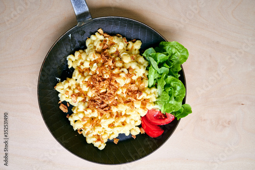 Bayrische Käsepätzle Kasspatzen mit Röstzwiebeln in einer Eisenpfanne auf einem Holztisch photo