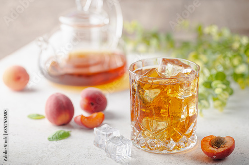 Glass of peach or apricot iced tea with fruit slices against white background