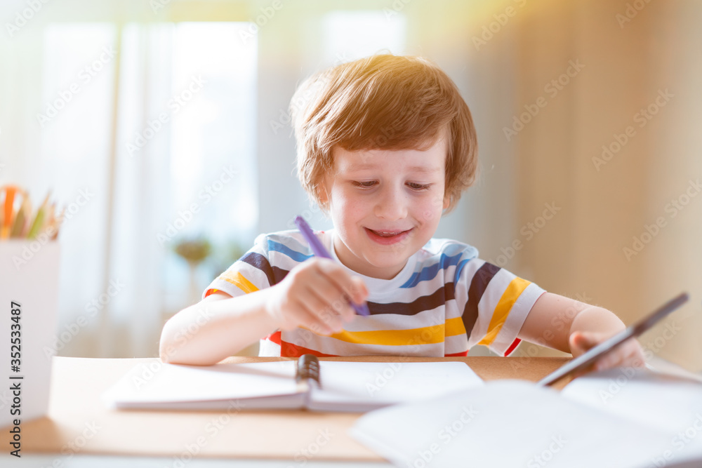 Distance learning online education. Caucasian smile kid boy studying at home with smartphone and doing school homework. Thinking child siting at table with cell phone due coronavirus quarantine Distance learning online education. Caucasian smile kid boy studying at home with smartphone and doing school homework. Thinking child siting at table with cell phone due coronavirus quarantine