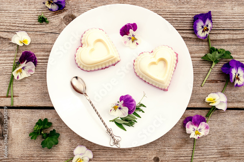 Souffle in the shape of a heart with cottage cheese  agar-agar and cream on a white plate on a wooden background.Violet flowers adorn the composition.  oncept of healthy food and healthy dessert 