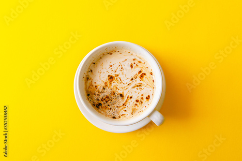 A cup of black coffee with milk and foam on yellow background.