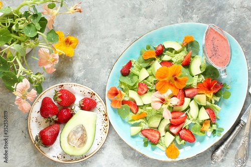 salad with nasturtium flowers and leaves with strawberries and avocados. dressed with strawberry vinaigrette or strawberry dressing with poppy seeds. edible flowers. top view, copy space