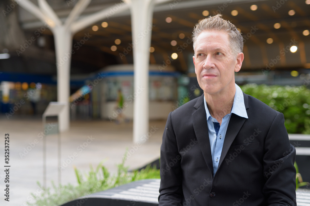 Mature businessman thinking and sitting in the city outdoors Mature businessman thinking and sitting in the city outdoors