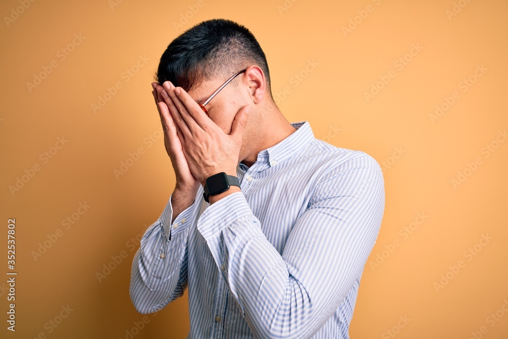 Young handsome hispanic business man wearing nerd glasses over yellow background with sad expression covering face with hands while crying. Depression concept. Young handsome hispanic business man wearing nerd glasses over yellow background with sad expression covering face with hands while crying. Depression concept.