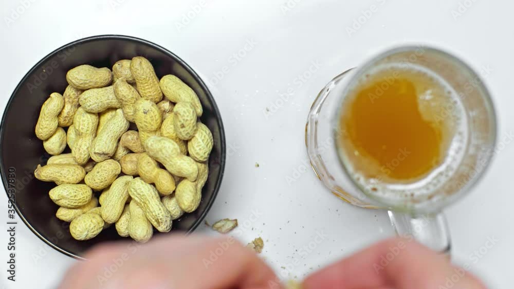 cropped view of man eating peanuts and drinking light beer on white table cropped view of man eating peanuts and drinking light beer on white table