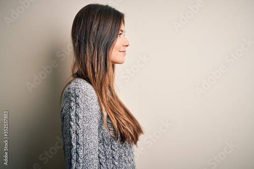 Young beautiful girl wearing casual sweater standing over isolated white background looking to side, relax profile pose with natural face with confident smile. © Krakenimages.com