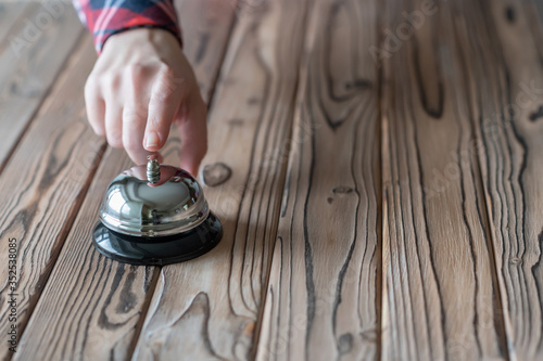 Hand of guest ringing silver vintage bell on wooden rustic reception desk with copy space. Hotel, restaurant.