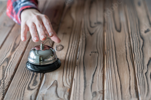 Hand of guest ringing in silver bell. on wooden rustic reception desk with copy space. Hotel service. Selective focus