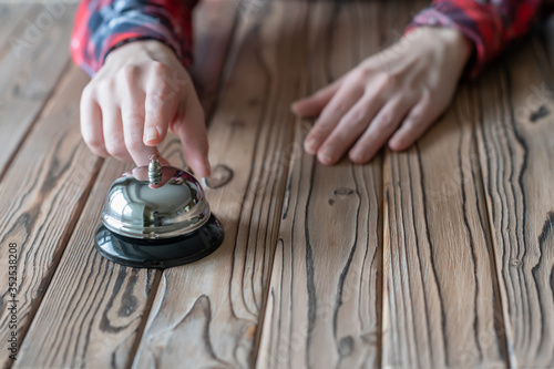 Hand of guest ringing in silver bell. on wooden rustic reception desk with copy space. Hotel, restaurant service. Selective focus