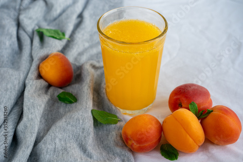 Glass of orange juice surrounded by ripe apricots on textile surface