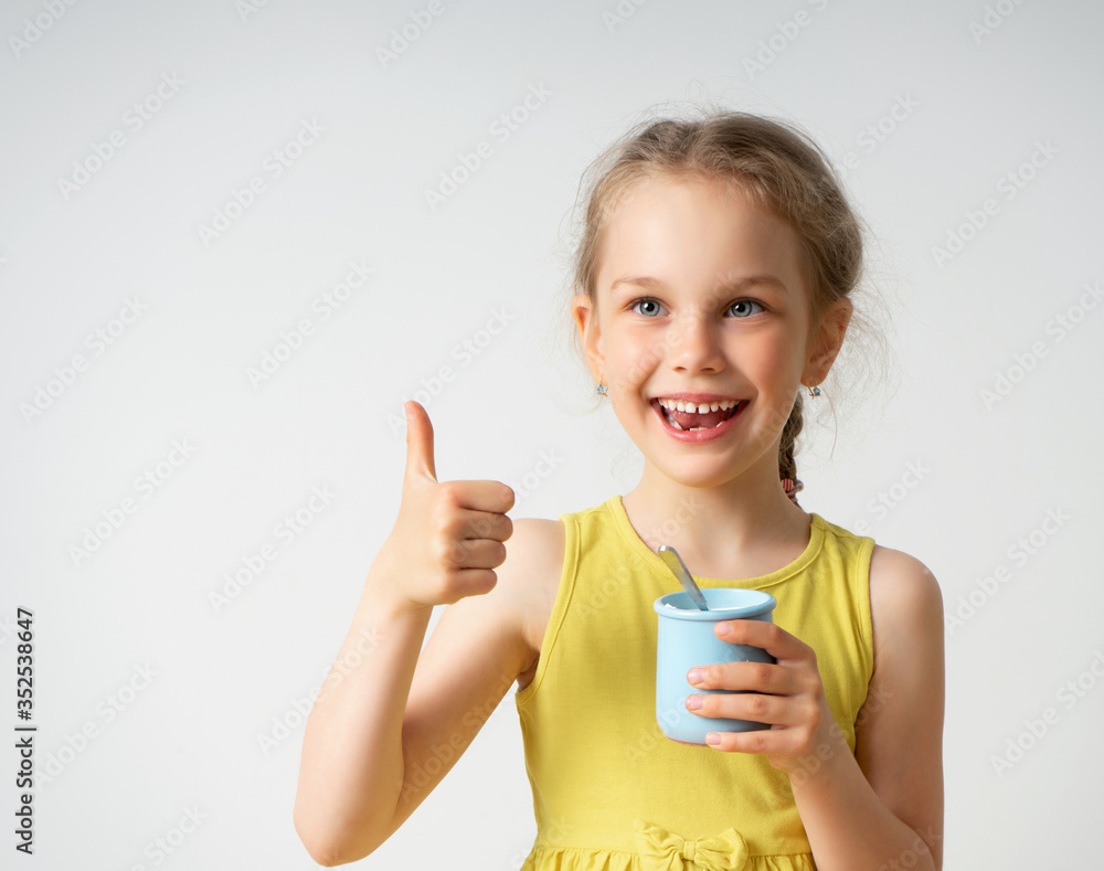 Happy little blonde girl in yellow clothing is delighted with tasty food showing shiny smile and thumb up gesture. Childhood, emotions, gesturing, healthy meal. Close up portrait isolated on white Happy little blonde girl in yellow clothing is delighted with tasty food showing shiny smile and thumb up gesture. Childhood, emotions, gesturing, healthy meal. Close up portrait isolated on white
