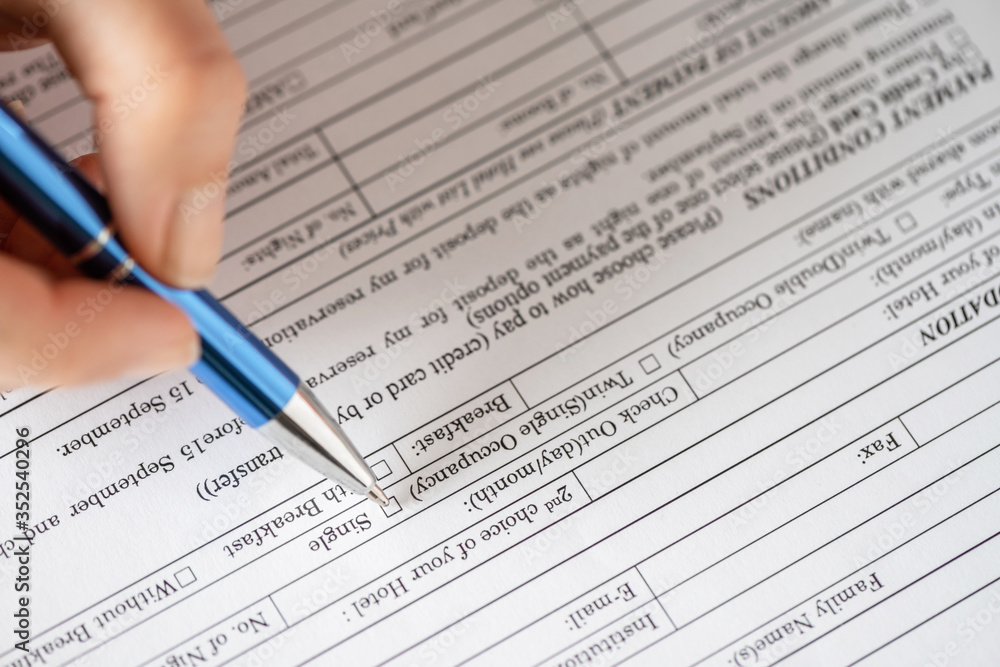 Woman filling hotel reservation form putting check mark on room type. Reception desk. Hotel service, registration. Close up. Selective focus. Woman filling hotel reservation form putting check mark on room type. Reception desk. Hotel service, registration. Close up. Selective focus.