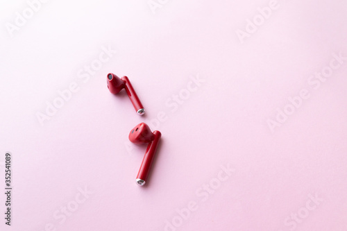 Red wireless headphones on pink background with copy space