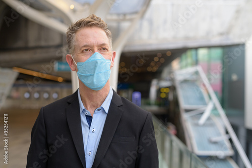 Mature businessman thinking with mask for protection from corona virus outbreak at the footbridge