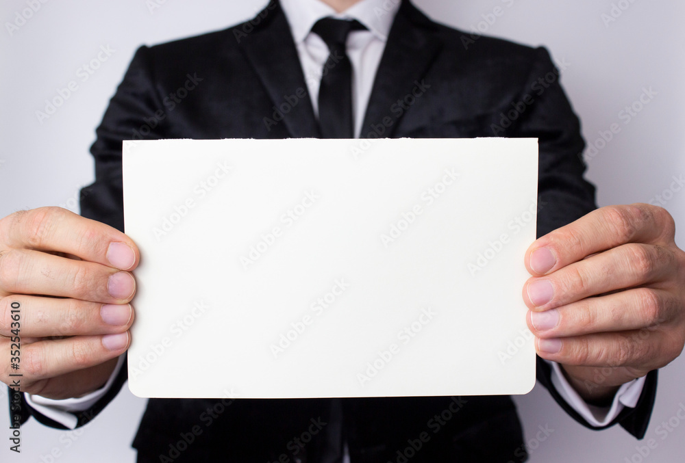 A young businessman holds in his hands an empty sheet of paper on a white background. A place for your advertising in business. A young businessman holds in his hands an empty sheet of paper on a white background. A place for your advertising in business.