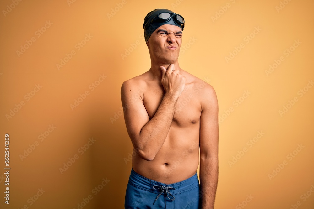 Young handsome man shirtless wearing swimsuit and swim cap over isolated yellow background Touching painful neck, sore throat for flu, clod and infection