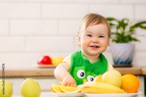 Happy child girl in the kitchen eats tasty fruits, sweet oranges.
