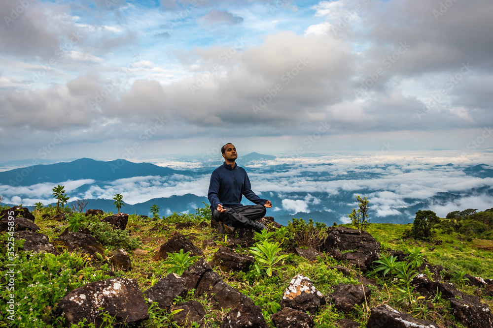 Fototapeta premium man meditating on rock isolated at the serene nature with amazing cloud layers in background