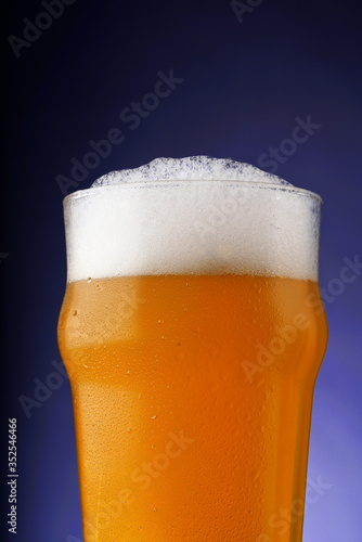 A pint of beer with foam in a glass with water drops on a dark background with gradient lighting