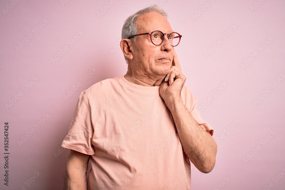 Grey haired senior man wearing glasses standing over pink isolated background with hand on chin thinking about question, pensive expression. Smiling with thoughtful face. Doubt concept. Grey haired senior man wearing glasses standing over pink isolated background with hand on chin thinking about question, pensive expression. Smiling with thoughtful face. Doubt concept.