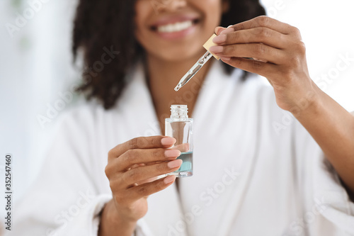Beauty And Skincare. Smiling Black Woman Holding Bottle With Moisturizing Face Serum photo