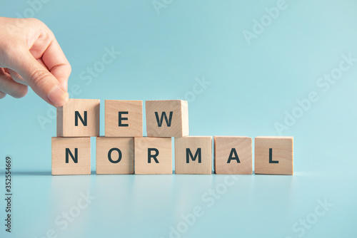 Woman hand flipping wooden cubes with NEW NORMAL word. Adapting to new life or business post-lockdown after coronavirus pandemic. Business with social distancing personal hygiene.