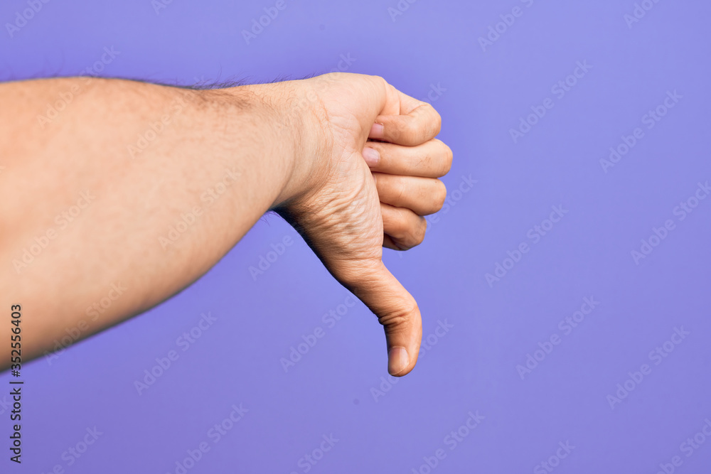 Hand of caucasian young man showing fingers over isolated purple background doing thumbs down rejection gesture, disapproval dislike and negative sign Hand of caucasian young man showing fingers over isolated purple background doing thumbs down rejection gesture, disapproval dislike and negative sign
