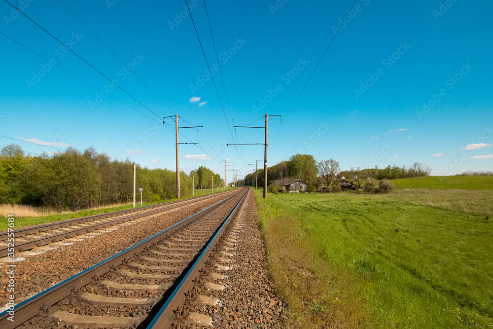 Summer landscape: old blue sky and clouds, green grass and trees, railway path road and old rusty industrial metal construction. A bright scenery view and spirit of adventure.