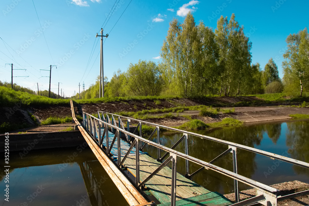 Pleasant summer landscape: old blue sky and clouds, green grass and a river lake artificial channel and an old industrial bridge.