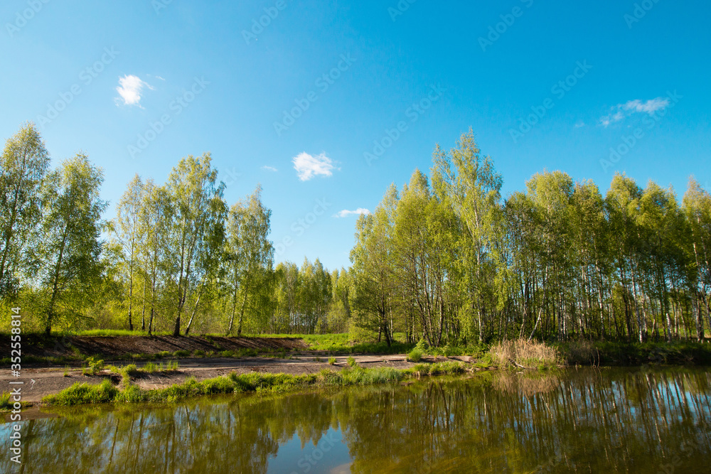 Pleasant summer landscape: old blue sky and clouds, green grass and a river lake artificial channel. A happy idyllic scenery view.