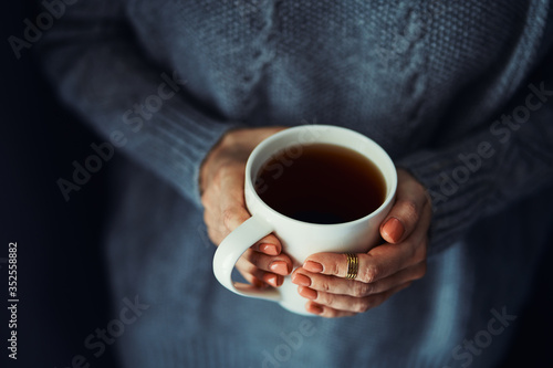 Cozy home. Female hands holding hot cup of coffee or tea.