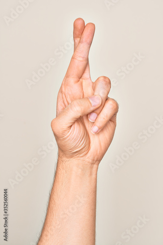 Hand of caucasian young man showing fingers over isolated white background gesturing fingers crossed, superstition and lucky gesture, lucky and hope expression © Krakenimages.com