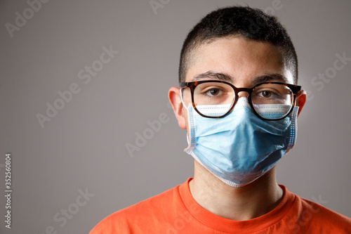 Ritratto di ragazzo giovane con occhiali da vista , maglia arancione e mascherina chirurgica , isolato su sfondo grigio photo