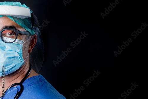 Medico  con mascherina chirurgica , visiera in plastica, guanti in lattice e camice blu isolato su sfondo nero photo