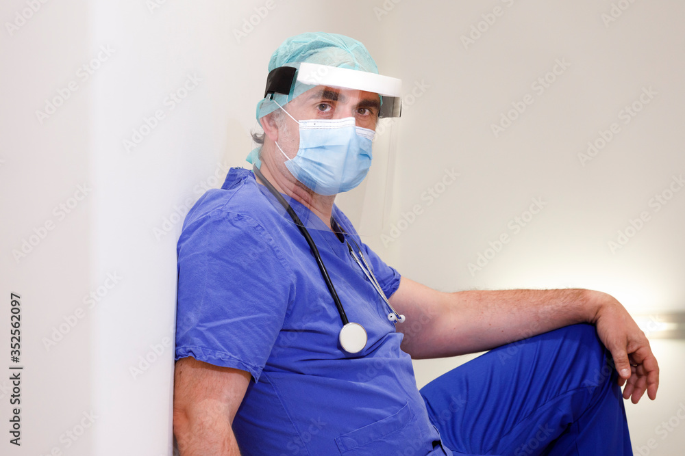 Chirurgo con mascherina e visiera in camice blu seduto disperato nella  corsia di un ospedale Stock 写真 | Adobe Stock
