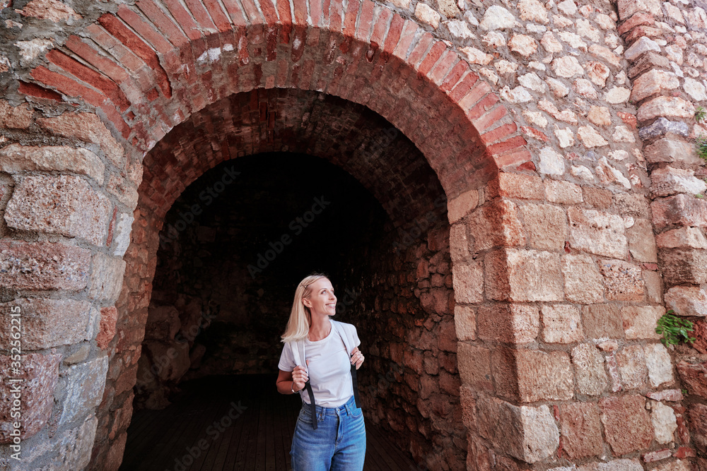 Young traveling woman with rucksack walking in ancient fortress.