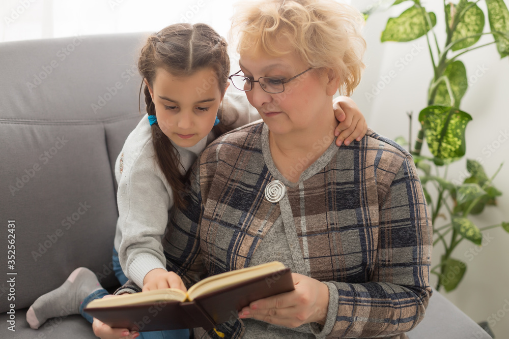 happy little girl and grandmother sit on couch and read book together happy little girl and grandmother sit on couch and read book together