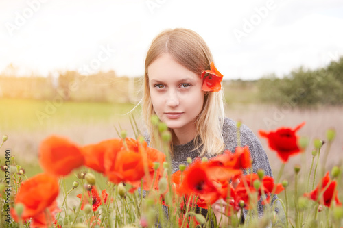 Beautiful young girl 18 years old blonde in a poppy field. Spring day in the village, a girl in the sun, a red poppy flower in her hair.