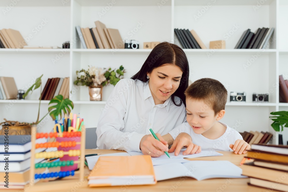 Young female tutor helping little elementary school boy with homework during individual lesson at home Young female tutor helping little elementary school boy with homework during individual lesson at home