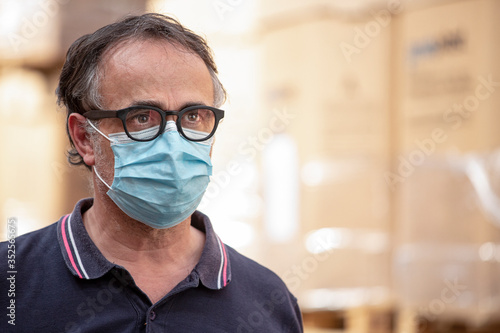 Ritratto di Uomo con occhiali neri e mascherina protettiva  nel magazzino in cui lavora photo