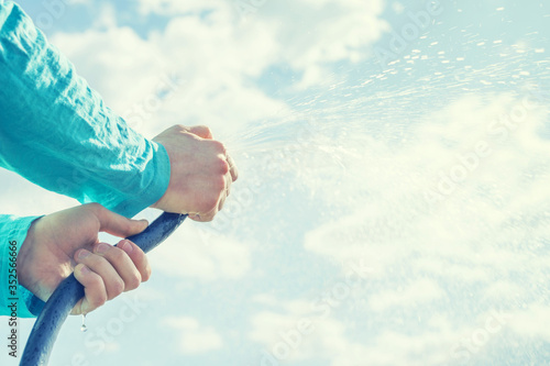 Hands of the child hold a hose with water against the sky, watering, splashing water © isavira