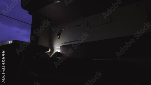 Timelapse man goes to bed to sleep inside compartment of corridor coach of railway passenger train. Railroad carriage wagon going at night. Travel and tourism concept. Interior, transportation. Window photo