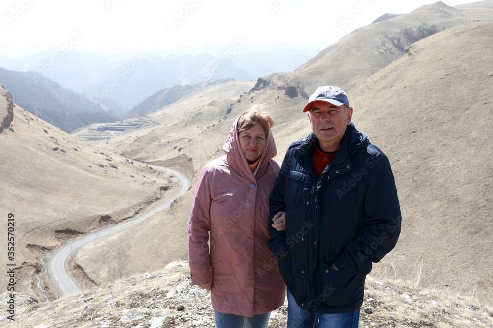 Senior couple on rocky ridge of Caucasus background