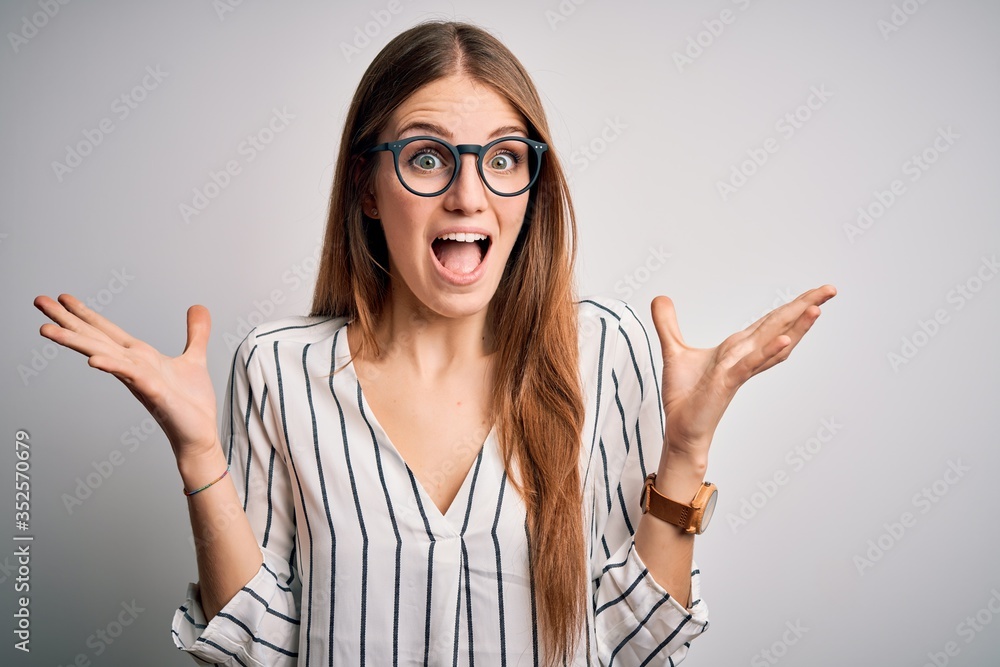 Young beautiful redhead woman wearing casual striped t-shirt and glasses celebrating crazy and amazed for success with arms raised and open eyes screaming excited. Winner concept Young beautiful redhead woman wearing casual striped t-shirt and glasses celebrating crazy and amazed for success with arms raised and open eyes screaming excited. Winner concept