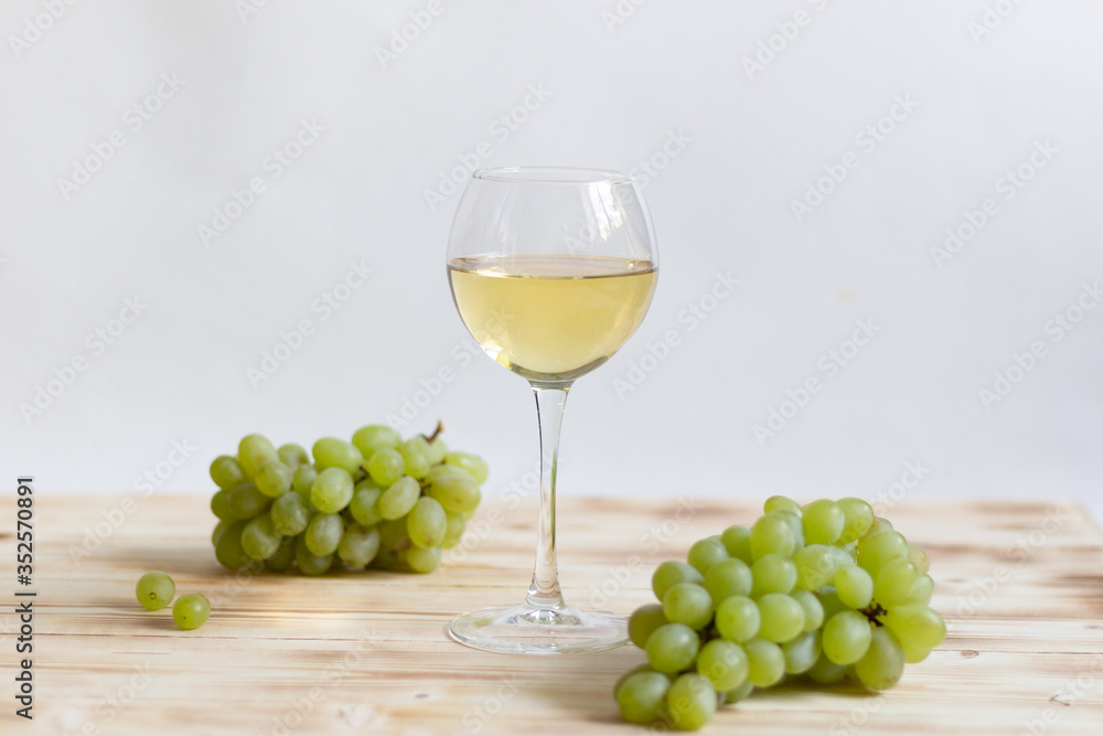 Glass of white wine and green grape bunches on wooden table Glass of white wine and green grape bunches on wooden table