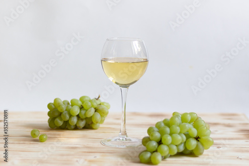 Glass of white wine and green grape bunches on wooden table