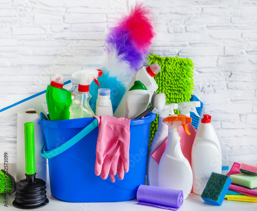 Foto Bucket with bottles of detergent and cleaning tools over white brick background