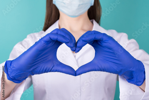 Close-up cropped photo of female doctor in white coat uniform rubber latex blue gloves making showing heart with her hands isolated on blue teal turquoise background